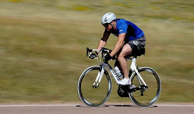 "Man cycling outdoors in blue jersey and helmet, performing cardio workout to boost endurance and support fat burning."