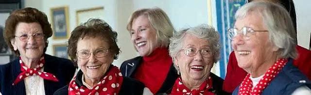 Group of smiling elderly women wearing red polka-dot scarves, enjoying a cheerful moment together, symbolizing stress-free living, emotional wellness, and the power of social connection.