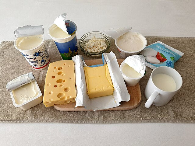 A variety of high-protein, low-carb dairy foods including cheese, butter, cottage cheese, yogurt, cream, and a mug of milk displayed on a wooden board—ideal choices for a low-carb, high-protein diet.